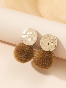 Detail van gehamerde metalen oorbellen met zachte bruine pluche pompons voor de herfst