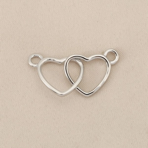 Vista macro de conector de doble corazón plateado con bucles para creación de joyas