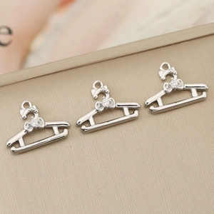 Detail van drie zilveren hanger-bedeltjes met strikjes en zirkoon op een beige bord