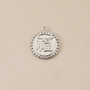 Macro shot of silver Fu character pendant with beaded edge on beige fabric background