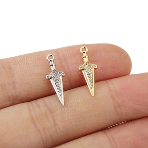 Dettaglio di ciondoli a spada in oro e argento con zirconi presentati su un dito