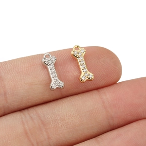 Makroaufnahme kleiner Gold- und Silber-Knochenanhänger mit Zirkon-Inlay auf dem Finger
