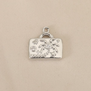 Macro view of silver suitcase pendant with palm tree relief and sparkling zircon inlay