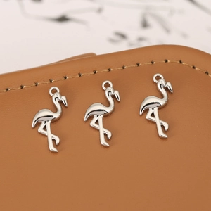 Three polished silver flamingo pendants for DIY jewelry making on brown leather background