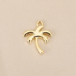 Detailed macro view of gold-plated palm tree pendant on a textured beige fabric background