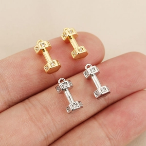 Macro shot showing small 18k gold plated dumbbell pendants with micro-pave zircons on fingertips