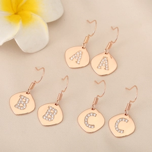 Close-up of three pairs of rose gold alphabet earrings with crystal A, B, C charms