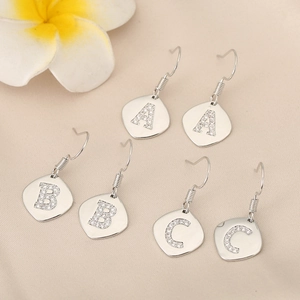 Close-up of vintage silver alphabet earrings with sparkling crystals on beige fabric