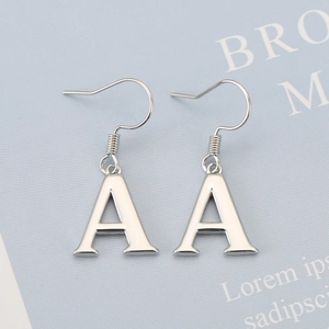 Close-up of silver letter A charm earrings with polished mirror finish on a blue card