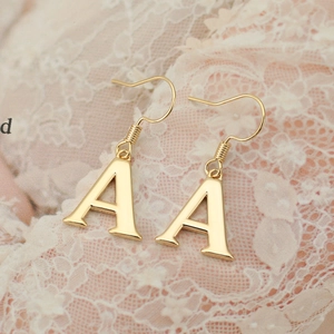 Macro shot of gold letter A drop earrings with wire wrapping on white lace fabric