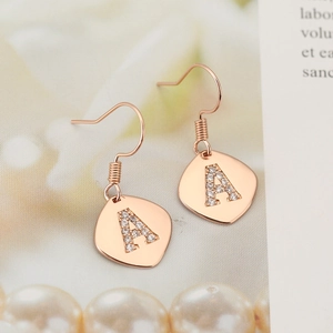 Close-up of rose gold letter A earrings with pave crystals on a vintage shield charm