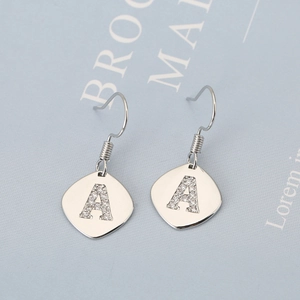 Macro detail of silver-toned metal earrings featuring a diamond-set letter A design