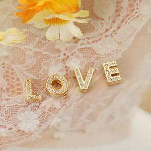 Close-up of gold LOVE letter charms with pavé cubic zirconia on white lace fabric