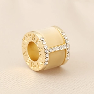 Macro detail of H-shaped gold-plated bead with beige enamel, crystals and Beauty engraving