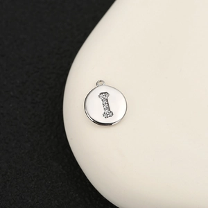 Detalle de un colgante redondo de cobre plateado con una letra I de piedras brillantes