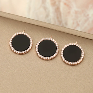 Three round 18K gold pendants with black enamel and micro-pave crystals on a metal tray