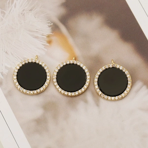 Macro view of three circular 18K gold-plated pendants with black enamel and zircons