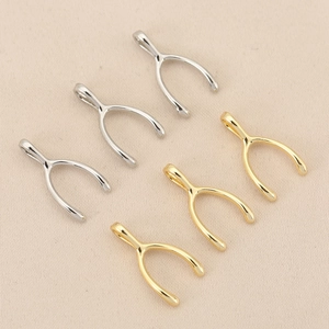 18K gold and silver plated wishbone charms set on beige textured fabric background