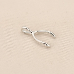 Polished silver wishbone shaped pendant on beige fabric background for jewelry making