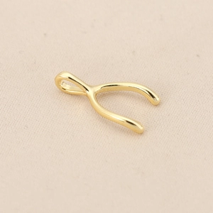 Macro view of polished 18K gold plated copper wishbone pendant on beige linen