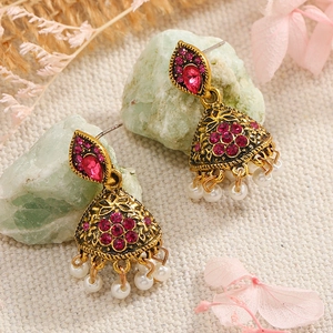 Detail of bohemian gold earrings with pink gemstones and white beads on natural stones