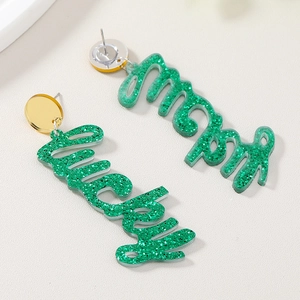 Grüne Glitzer Acryl Lucky und Merry Buchstaben Ohrringe auf beigefarbenem Hintergrund