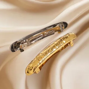 Hammered gold spring hair clip with minimalist metal texture on elegant satin background