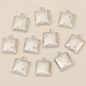 Macro shot of ten square silver-plated pendants with cubic zirconia on beige fabric