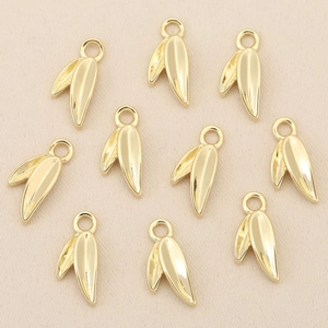 Macro detail of ten gold leaf charms for DIY jewelry making on a textured background