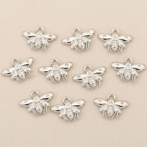 Macro view of ten small silver bee pendants with zircon inlay on textured fabric