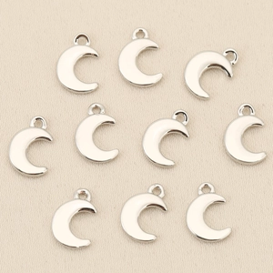 Detailed view of ten silver crescent moon pendants for DIY jewelry making on fabric