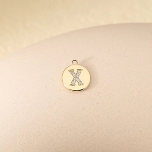 Detailed macro view of a gold-plated copper pendant featuring a cubic zirconia inlaid letter X