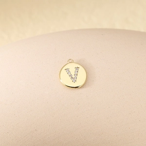 Macro view of golden round pendant with zircon letter V inlay on textured display stand