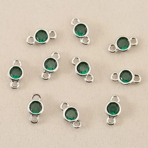 Close-up of circular green zircon pendants with silver plated dual-ring connectors for DIY jewelry