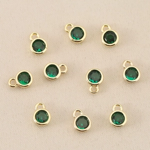 Makro-Detail von zehn vergoldeten runden Anhängern mit grünem Zirkon für DIY-Schmuck