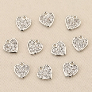 Macro detail of ten heart pendants with white zircons on a textured beige fabric background