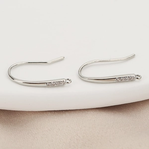 Detailed view of silver-plated earring hooks with cubic zirconia on champagne silk fabric