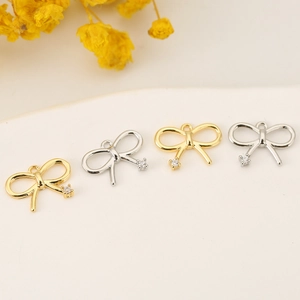 Primer plano de dijes de lazo dorado y plateado con pedrería para creación de joyas DIY