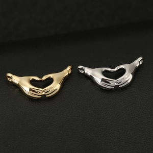 Close-up of 18K gold and silver hand heart pendants with high-polish mirror finish