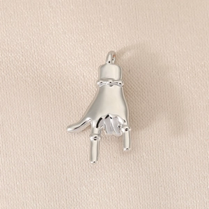 Close-up of polished silver metal hand gesture pendant on beige silk background