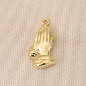 Detailed view of prayer hands gold pendant with hammered texture on beige fabric