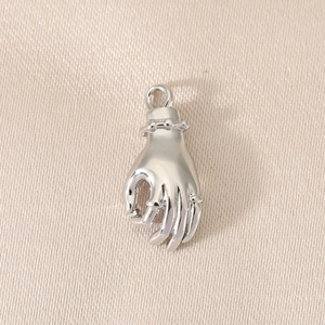 Macro detail of hand-shaped silver pendant charm with polished finish and beaded wrist