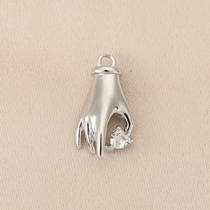 Macro detail of a silver hand-shaped pendant holding a heart-cut cubic zirconia stone