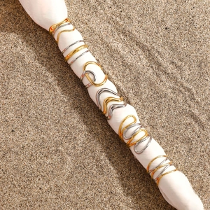 Detail of two-tone stainless steel wavy and hammered rings on white silk over sand