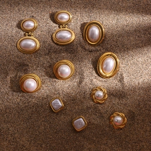 Collezione di orecchini vintage in oro e perle esposti su una superficie di sabbia