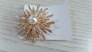 Détail d'une broche tournesol dorée avec une perle blanche et des strass étincelants
