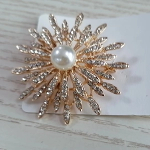 Broche tournesol dorée avec perle centrale et strass étincelants sur fond en bois