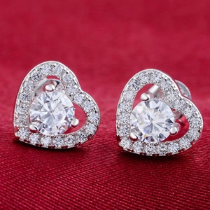Macro shot of silver heart-shaped stud earrings with round crystals on red silk