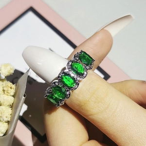 Close-up of a silver ring with an oval green zircon and pavé-set diamonds on finger