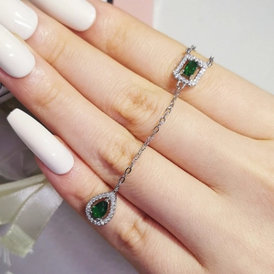 Detail of silver chain jewelry featuring emerald-cut and teardrop green gemstones with diamonds